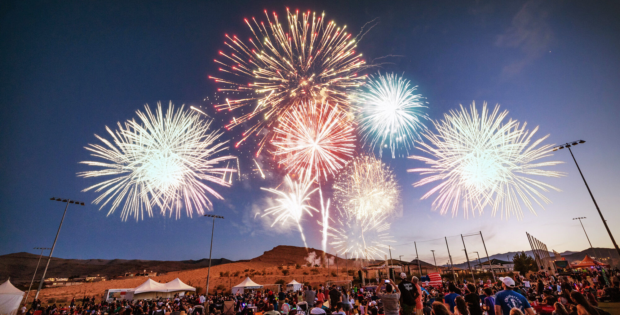 Vibrant fireworks display illuminating the night sky at a lively outdoor event.